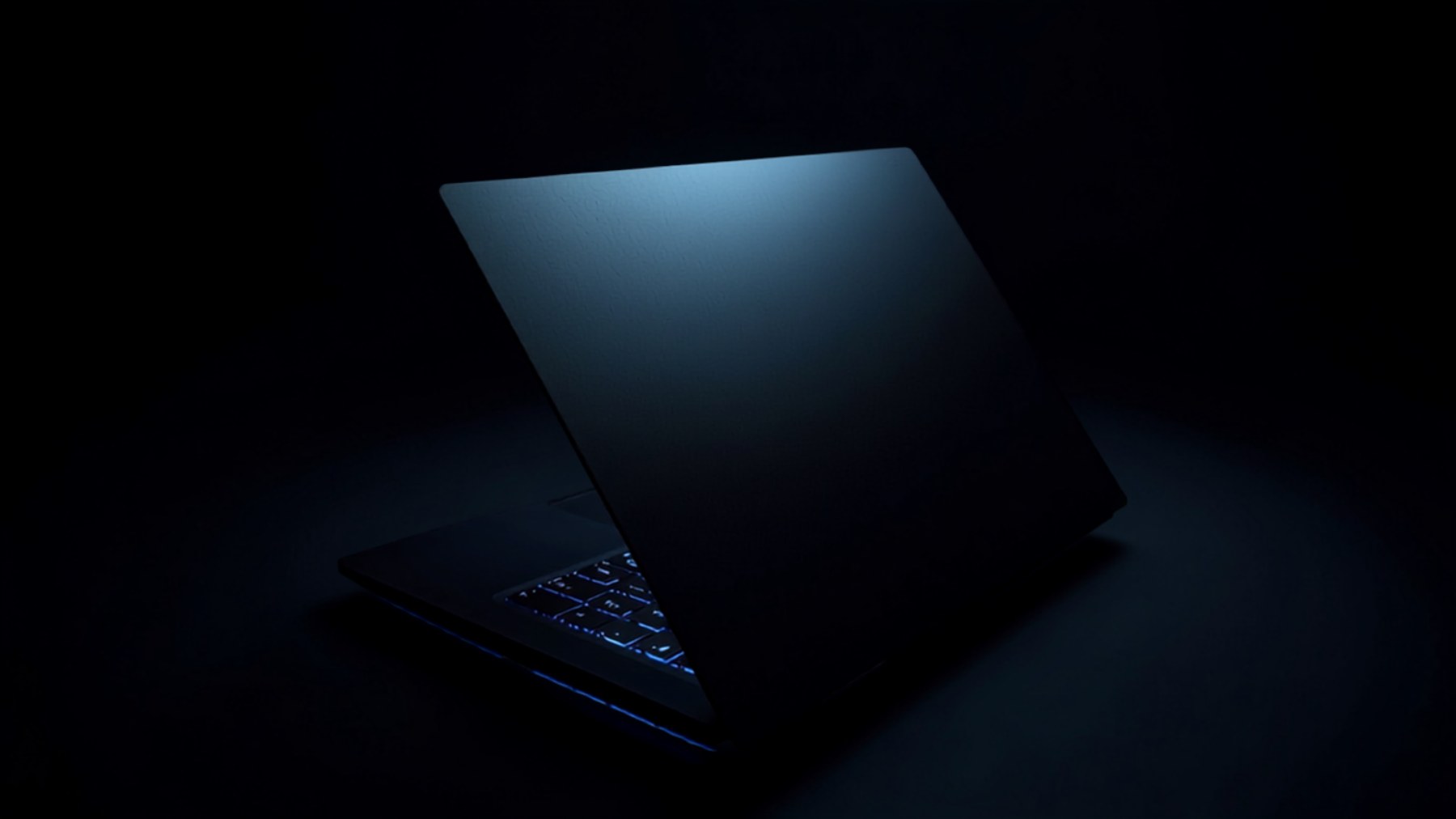 An open gaming laptop photographed from a rear three-quarter angle in a dark room, its lid lit in cool blue and keyboard backlighting glowing beneath